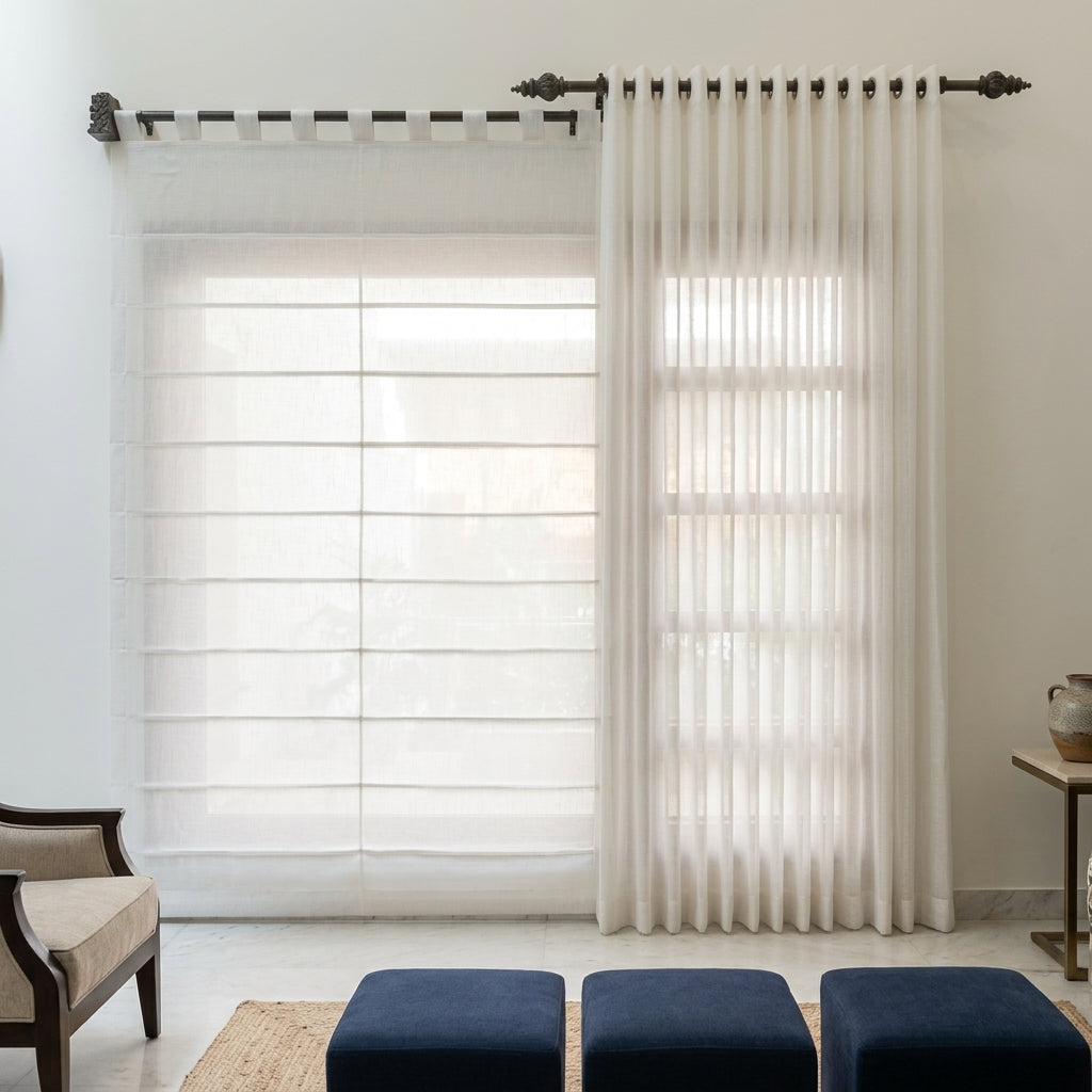 A pair of off-white sheer curtains hanging on a dark metal rod in a bright, modern room. The left side shows the curtains drawn as a Roman shade, while the right side shows a single panel with grommets hanging vertically.