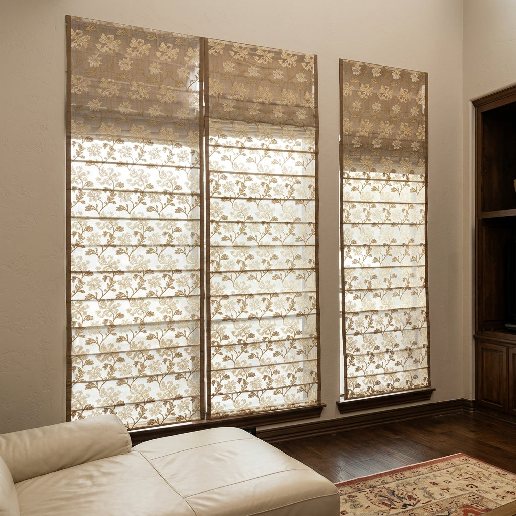 Three tall window treatments with sheer cream and beige floral-patterned Roman shades hanging in a room with wood flooring and a light-colored leather sofa partially visible in the foreground.