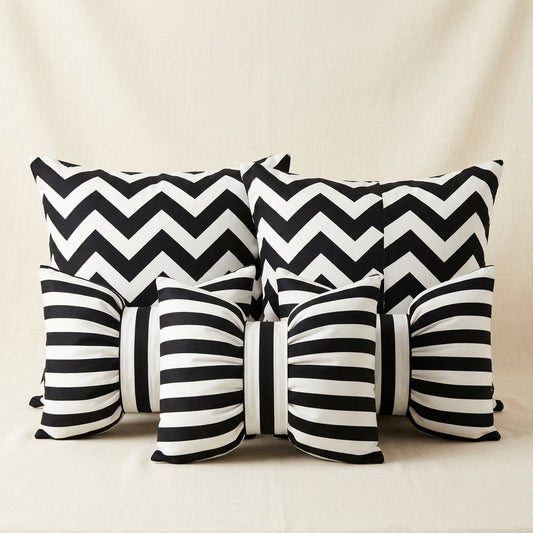A set of black and white patterned throw pillows, including two square pillows with a bold chevron design and three rectangular pillows with horizontal stripes and bow details, arranged on a neutral beige fabric background.