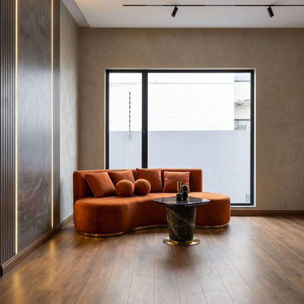 A modern curved orange sectional sofa with matching throw pillows in a minimalist living room featuring a dark marble coffee table and wood flooring.