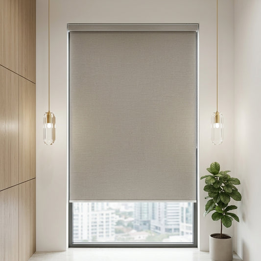 A beige roller blind with a textured fabric surface, partially rolled down over a modern window. The window is set in a bright room with a light wood paneled wall on the left, two hanging pendant lights with clear glass shades, and a potted green plant on the right.